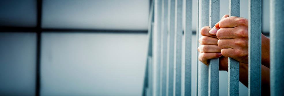 Hands grip the bars of a prison cell