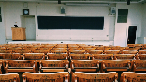 Empty lecture style classroom with podium, blackboard and wooden seats