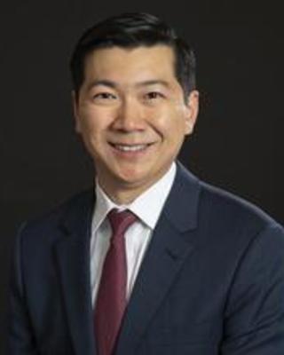 Smiling Asian man in a dark suit in front of a dark background