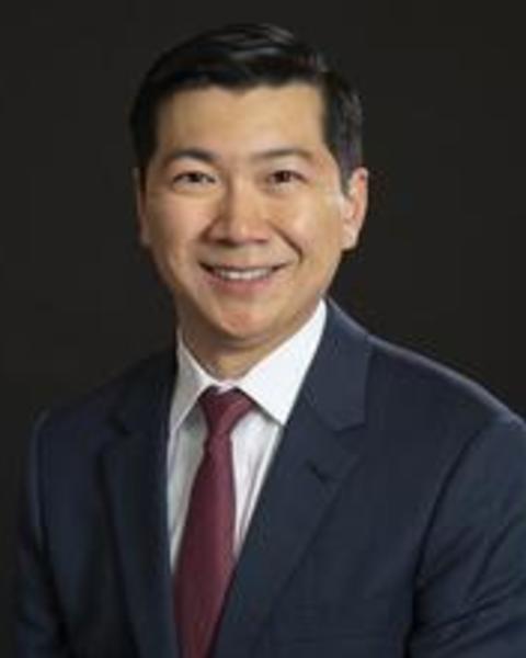 Smiling Asian man in a dark suit in front of a dark background